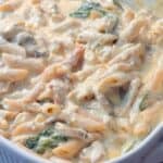 Close up shot of one pan creamy pasta bake with penne, mushrooms, spinach, and sun-dried tomatoes stirred together.