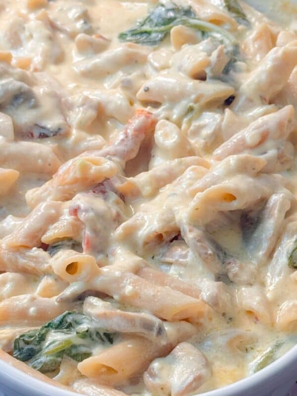 Close up shot of one pan creamy pasta bake with penne, mushrooms, spinach, and sun-dried tomatoes stirred together.