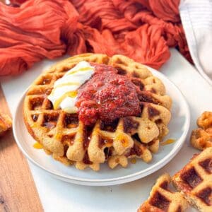 pumpkin spice protein waffle served on a plate, topped with a dollop of Greek yogurt, strawberry jam, and a drizzle of honey