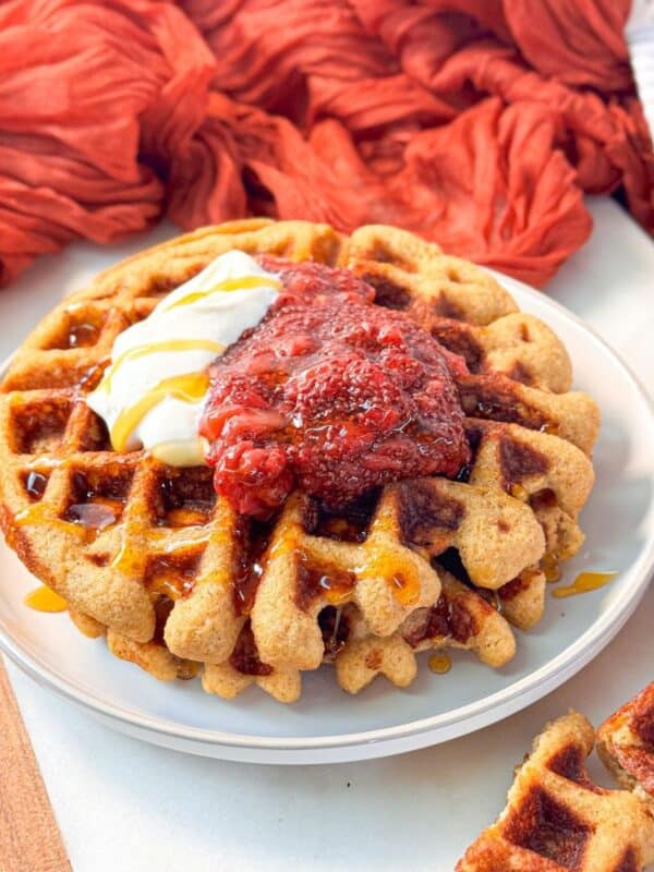 pumpkin spice protein waffle served on a plate, topped with a dollop of Greek yogurt, strawberry jam, and a drizzle of honey
