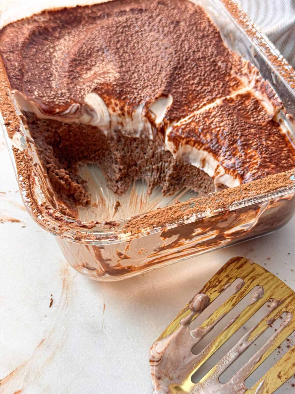 Rich Mocha Chia Pudding Cake Pirex dish of high protein mocha chia pudding cake topped with whipped cream and cocoa powder, partially scooped out.