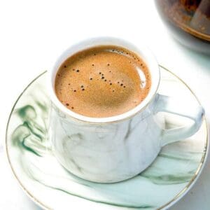 A close-up shot of a cup of Turkish coffee with rich foam served on a marble-patterned saucer.