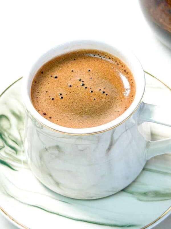 A close-up shot of a cup of Turkish coffee with rich foam served on a marble-patterned saucer.