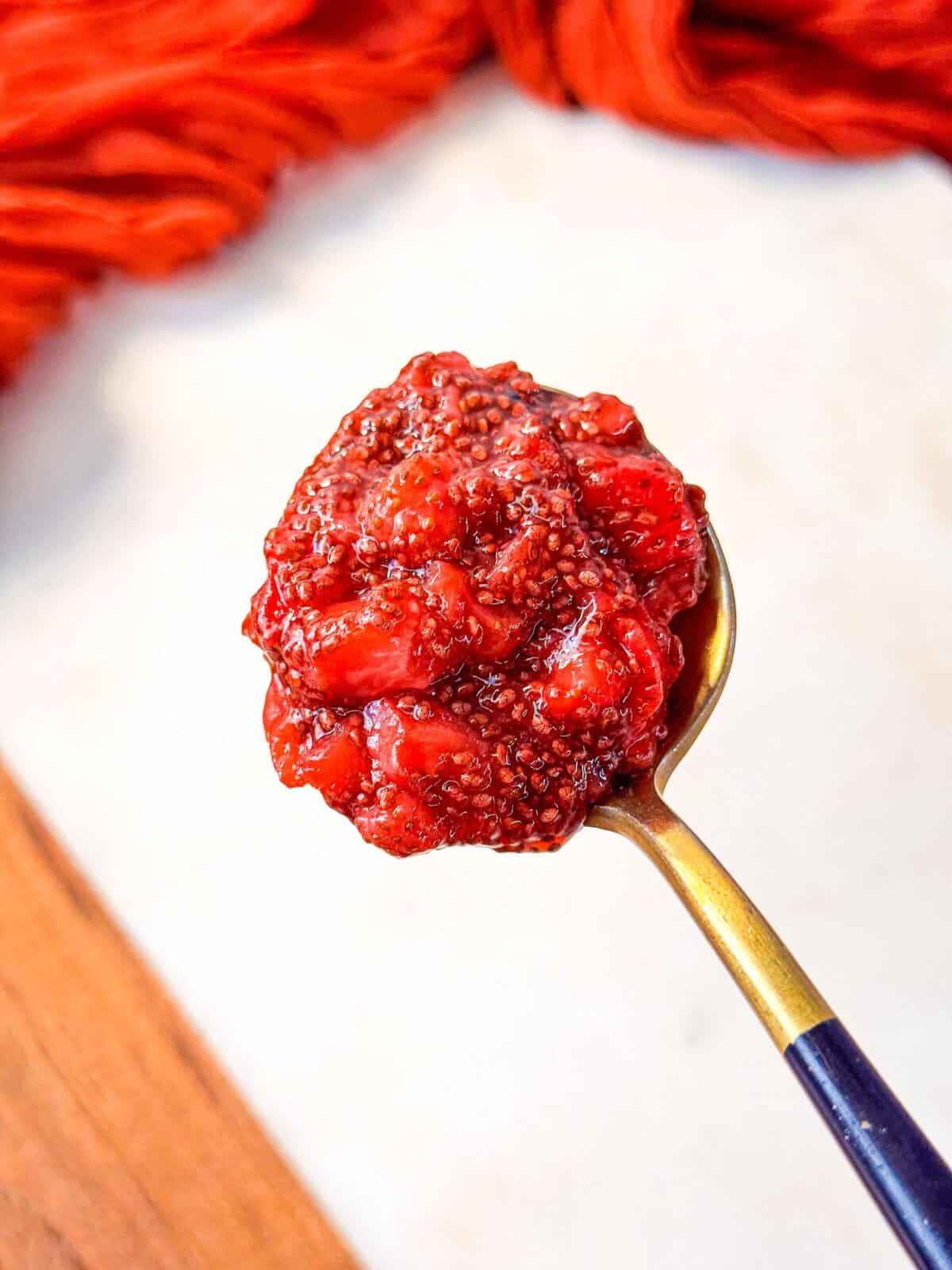Strawberry Chia Seed Jam a close up shot of a spoonful of homemade strawberry chia jam with visible chia seeds and strawberry chunks.