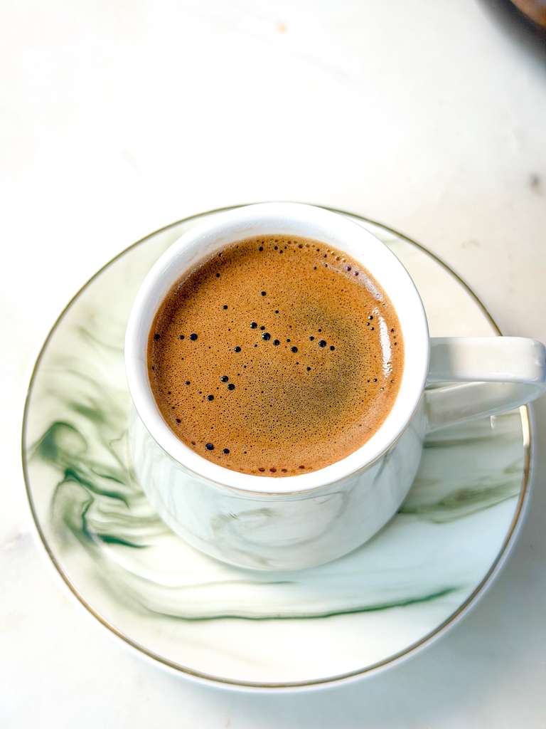 Best Turkish Coffee A top shot of a cup of Turkish coffee with rich foam served on a marble-patterned saucer.
