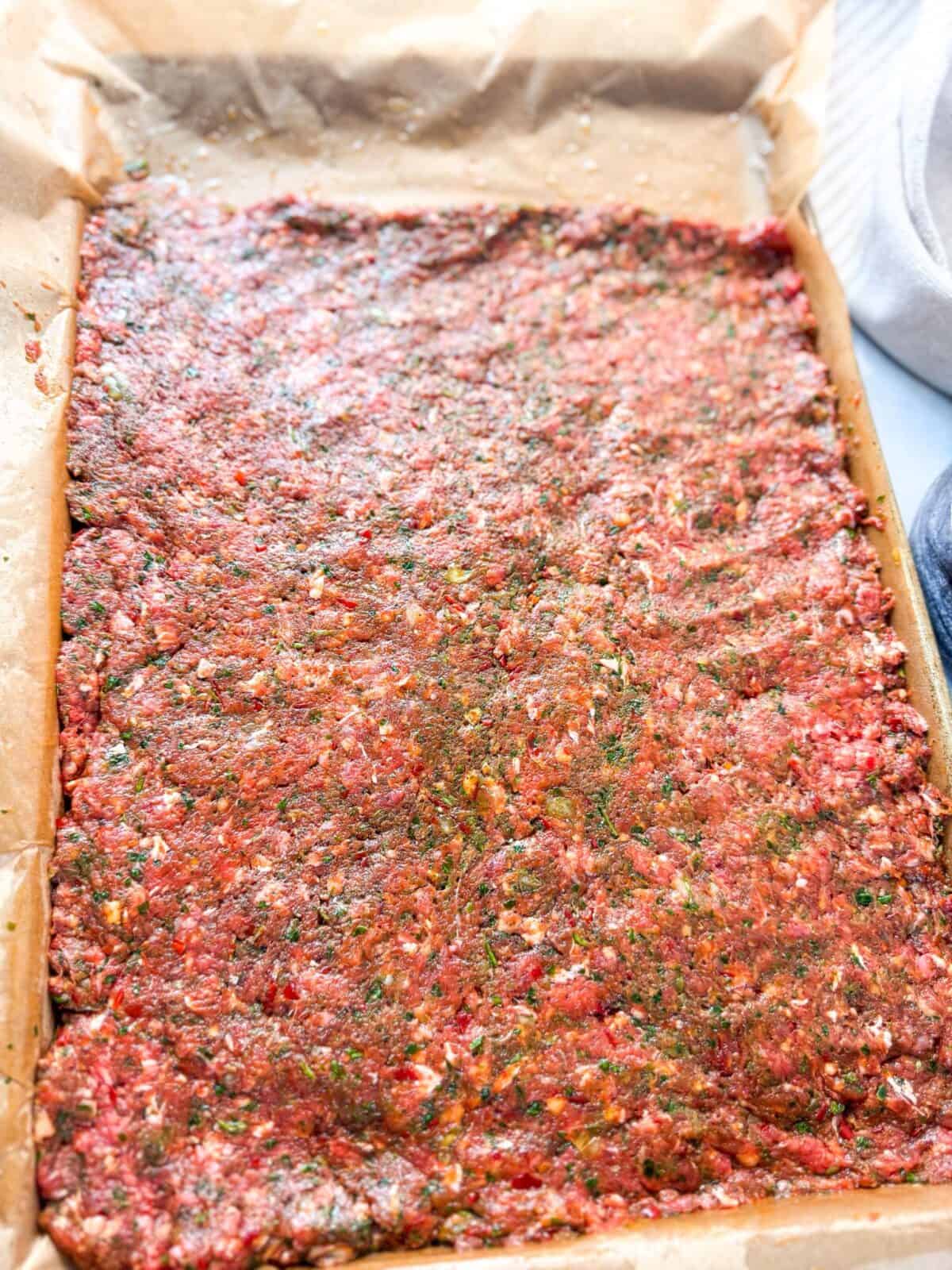 How to Make Baked Sheet Pan Kebabs seasoned raw ground beef mixture spread evenly on a parchment-lined sheet pan, ready to be baked for sheet pan kebabs