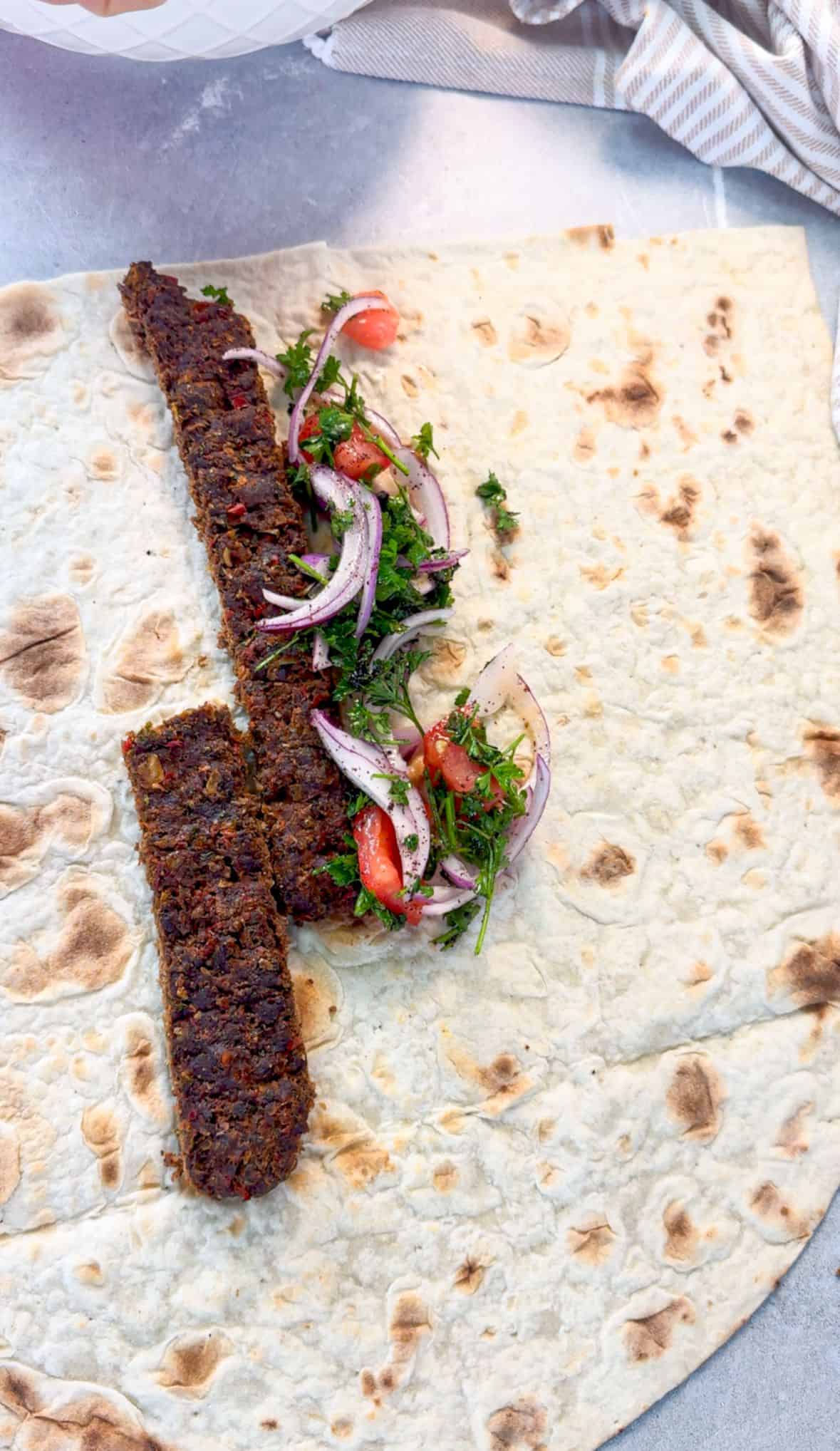 Make Baked Sheet Pan Kebabs Baked kafta kebabs served on flatbread with parsley, tomato, and red onion salad, ready to be wrapped