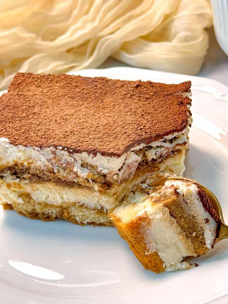 Homemade Tiramisu Egg Free a slice of eggless tiramisu on a white plate, with one bite out