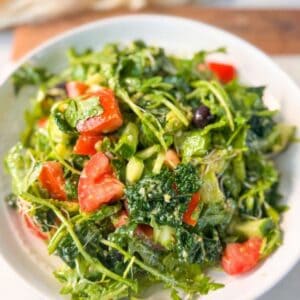 A vibrant Mediterranean arugula salad with diced tomatoes, cucumber, kale, and olives tossed in a Dijon dressing