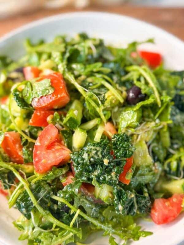 A vibrant Mediterranean arugula salad with diced tomatoes, cucumber, kale, and olives tossed in a Dijon dressing