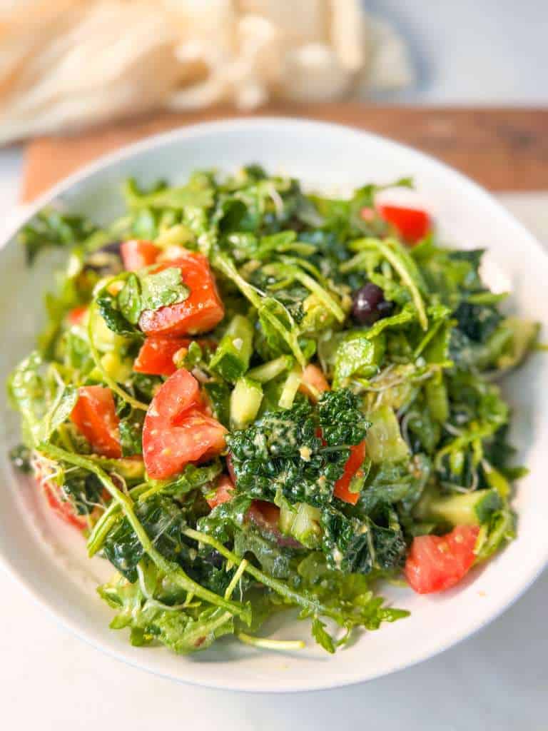 Mediterranean Arugula Salad with Dijon Dressing A vibrant Mediterranean arugula salad with diced tomatoes, cucumber, kale, and olives tossed in a tangy Dijon vinaigrette, served on a white plate