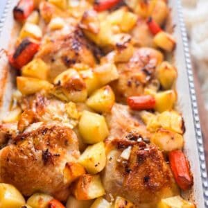baking dish filled with roasted chicken thighs, golden potatoes, and caramelized carrots
