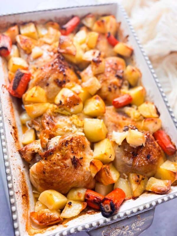 a large baking dish filled with juicy golden lemon garlic roasted chicken thighs, tender potatoes, and caramelized carrots