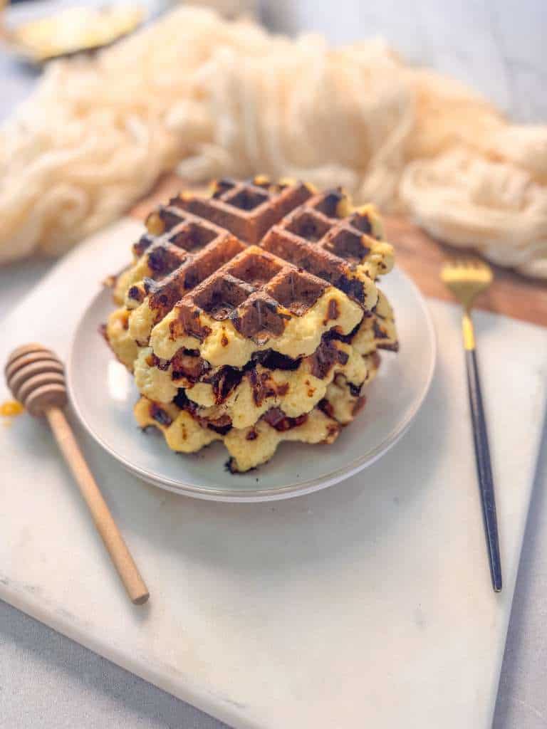 Fluffy Cottage Cheese Waffles Fluffy cottage cheese waffles stacked on a small plate, served on a marble board with a honey dipper and fork beside them.