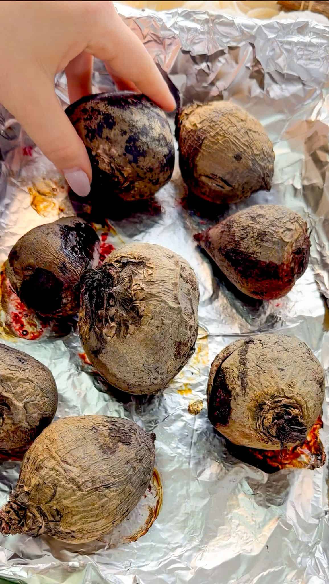 How to Roast Beets Roasted beet over a foil-lined baking dish filled with whole roasted beets, and a woman tries to hold one beet.
