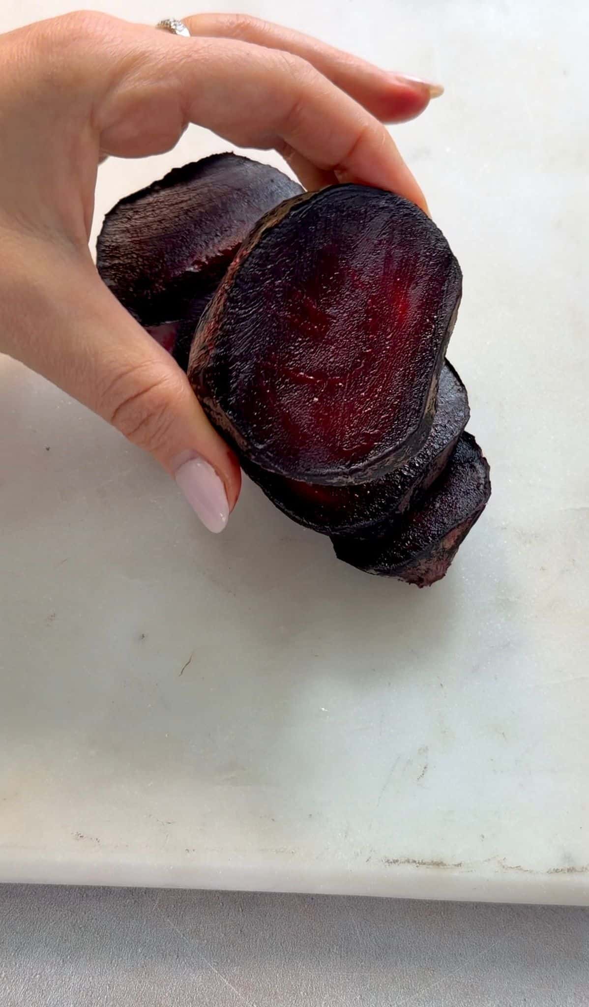 Oven Roasted Beets Hand holding a half of a peeled roasted beet while the other half appears in the background.