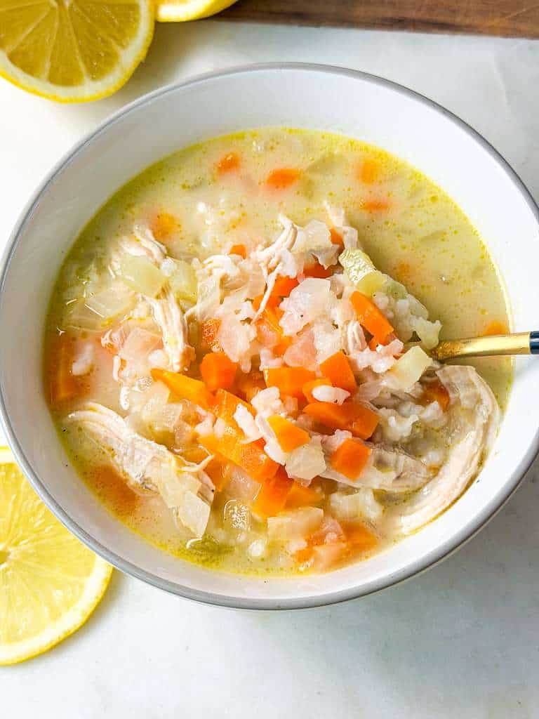 The Best Chicken Lemon Rice Soup Top shot of a spoonful of lemon chicken rice soup showing shredded chicken, carrots, and rice in a creamy broth.