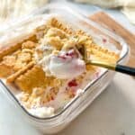Spoon scooping creamy no bake viral Japanese strawberry cheesecake layered with biscuits from a glass dish.