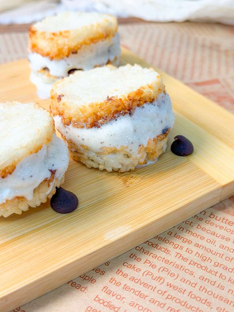 Crispy Rice Ice Cream Sandwiches close up shot of crispy rice ice cream sandwiches with vanilla filling on a wooden board, with chocolate chips scattered around
