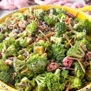 close-up shot of fresh broccoli salad with crunchy vegetables, dried cranberries, pumpkin seeds, and creamy blue cheese dressing served in a yellow bowl.