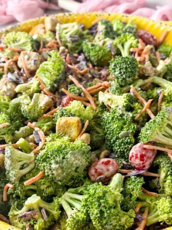 close-up shot of fresh broccoli salad with crunchy vegetables, dried cranberries, pumpkin seeds, and creamy blue cheese dressing served in a yellow bowl.