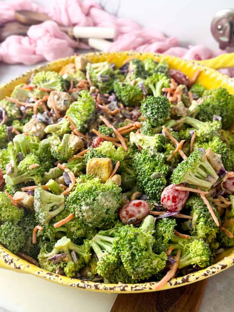 Creamy Broccoli Crunch Salad with Blue Cheese Dressing Fresh broccoli salad with crunchy vegetables, dried cranberries, pumpkin seeds, and creamy blue cheese dressing served in a yellow bowl.