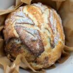 Top shot of golden crust artisan sourdough bread baked in a Dutch oven with rustic scoring and flour-dusted top