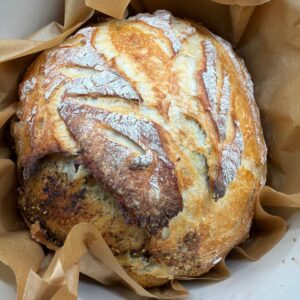 Top shot of golden crust artisan sourdough bread baked in a Dutch oven with rustic scoring and flour-dusted top